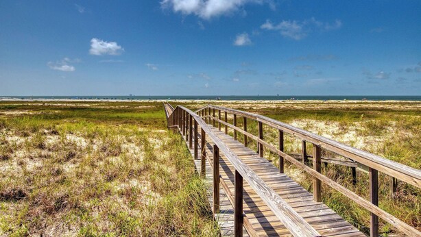 Une promenade en bois qui mène à une plage, avec un ciel dégagé.