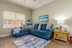 A living room with a sectional sofa, a patterned rug, a side table with a lamp, and a painting on the wall.