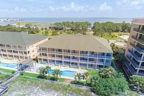 A multi-story hotel with a pool area, balconies, and a view of the ocean and bridge.