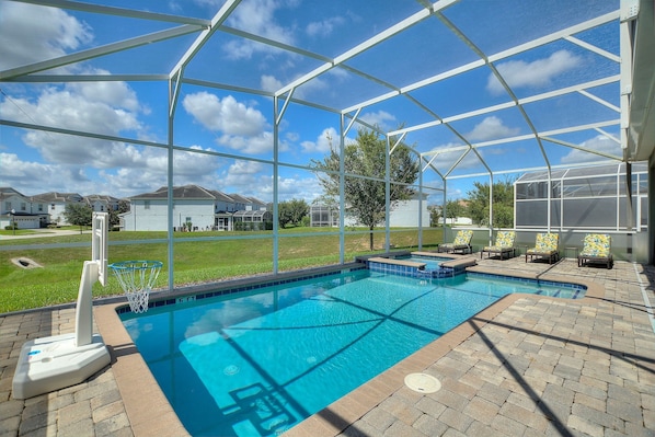 Une piscine couverte avec un panier de basketball, des chaises longues et une vue sur les maisons au loin.