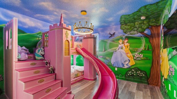 Ein Spielzimmer für Kinder mit einem rosa Schloss, einer Rutsche und einer Wandmalerei von Prinzessinnen.