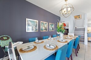 Un coin repas avec une longue table dressée pour six personnes, des chaises bleues et un lustre.