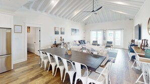 A spacious kitchen with a dining area, a living room with a sofa and coffee table, and a large window providing natural light. - 2 dog-friendly beach houses right on the sand w/private heated pool & elevator (Dauphin Island)