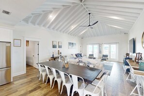 A spacious kitchen with a dining area, a living room with a sofa and coffee table, and a large window providing natural light. - 2 dog-friendly beach houses right on the sand w/private heated pool & elevator (Dauphin Island)
