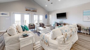A spacious living room with a ceiling fan, a flat-screen TV, and a large window. - 2 dog-friendly beach houses right on the sand w/private heated pool & elevator (Dauphin Island)