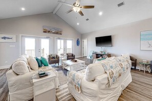A spacious living room with a ceiling fan, a flat-screen TV, and a large window. - 2 dog-friendly beach houses right on the sand w/private heated pool & elevator (Dauphin Island)