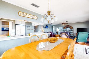 A dining area with a wooden table, chairs, a chandelier, and a 'BEACH HOUSE' sign. - Dog-Friendly Bayfront Getaway w/ Two Kitchens, Free WiFi, & a Great Location! (Dauphin Island)