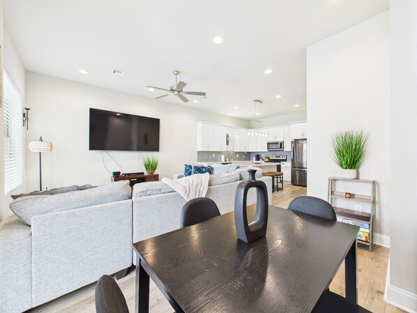 A modern living room with a grey sofa, a black dining table, and a ceiling fan.