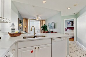 A kitchen with white cabinetry, a sink, and a ceiling fan. - Beachfront condo with stunning views, shared hot tub, fitness room, & indoor pool (Gulf Shores)