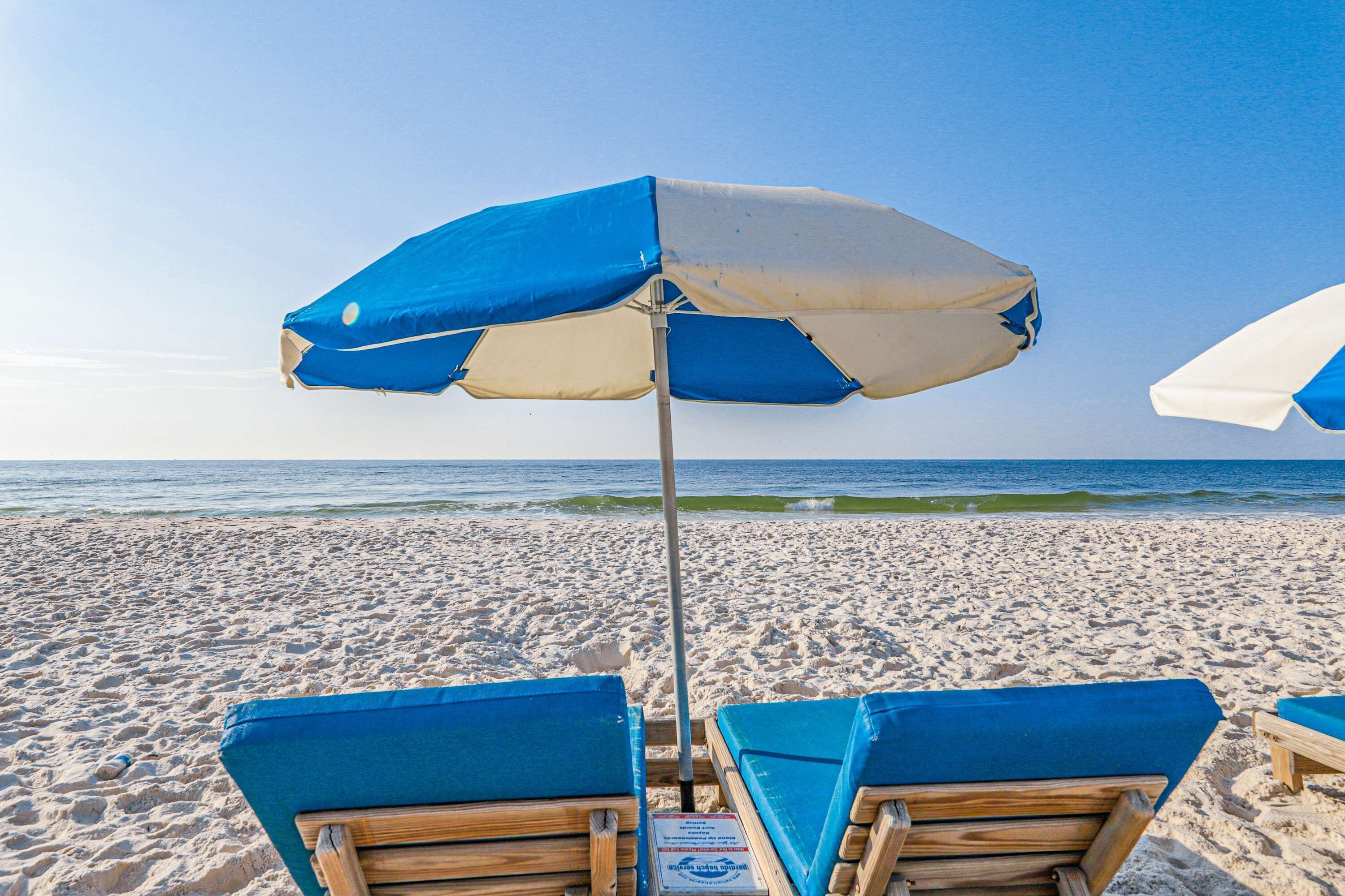 Una spiaggia con ombrelloni blu e bianchi, lettini di legno e l'oceano sullo sfondo.
