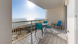 A balcony with a view of the sea, a table with chairs, and a railing. - Spacious beachfront condo with full kitchen, shared pool and beach access (Gulf Shores)