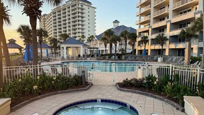 A hotel pool area with lounge chairs, a hot tub, and a view of high-rise buildings. - Spacious beachfront condo with full kitchen, shared pool and beach access (Gulf Shores)
