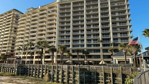 A multi-story hotel with balconies, palm trees, and an American flag. - Spacious beachfront condo with full kitchen, shared pool and beach access (Gulf Shores)