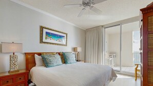A bedroom with a bed, a nightstand, a lamp, a picture on the wall, and a view of the outside. - Spacious beachfront condo with full kitchen, shared pool and beach access (Gulf Shores)