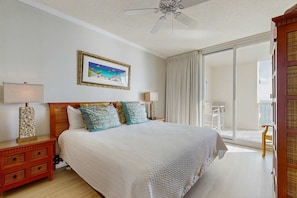 A bedroom with a bed, a nightstand, a lamp, a picture on the wall, and a view of the outside. - Spacious beachfront condo with full kitchen, shared pool and beach access (Gulf Shores)