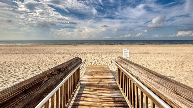 Een houten looppad dat naar een zandstrand leidt, onder een heldere lucht.