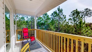 A covered porch with a wooden railing, a yellow table, and red chairs. - Peaceful hideaway with modern interior & spacious balcony - adjacent to the dune (Dauphin Island)