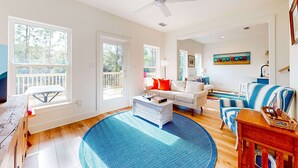 A spacious living room with a large window, a ceiling fan, and a dining area with a view of the deck. - Peaceful hideaway with modern interior & spacious balcony - adjacent to the dune (Dauphin Island)