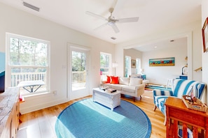 Uma sala de estar espaçosa com uma janela grande, ventilador de teto e área de jantar com vista para o deck.