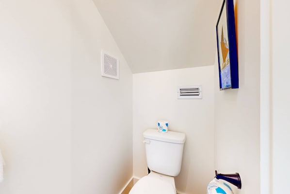 A bathroom with a toilet, a vent, and a framed picture on the wall.