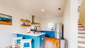 A modern kitchen with a central island, bar stools, a stainless steel refrigerator, and a colorful rug. - Peaceful hideaway with modern interior & spacious balcony - adjacent to the dune (Dauphin Island)
