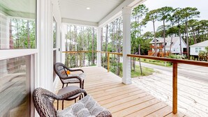 A covered porch with wicker chairs and a view of a residential street.
