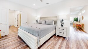 A bedroom with a bed, bedside tables, a ceiling fan, and a view into the adjacent dining area.