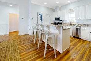 A modern kitchen with white cabinets, a granite countertop, stainless steel appliances, and a bar area with stools. - Inviting waterfront home with balcony, full kitchen, central AC, & W/D (Dauphin Island)