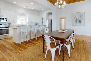 A modern kitchen with white cabinetry, a wooden dining table, and a woven rug. - Inviting waterfront home with balcony, full kitchen, central AC, & W/D (Dauphin Island)