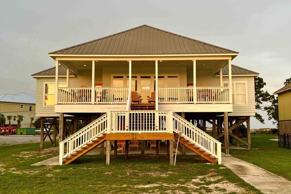 A two-story house with a balcony, wooden stairs, and a metal roof. - Inviting waterfront home with balcony, full kitchen, central AC, & W/D (Dauphin Island)