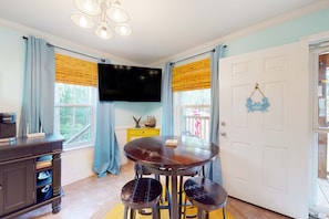 Un comedor con una mesa redonda, dos sillas, un televisor montado en la pared y una puerta decorada con azul.