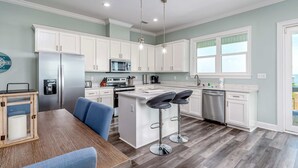 A modern kitchen with white cabinets, a central island with bar stools, a refrigerator, microwave, and a dishwasher. - Idyllic, dog-friendly Bay Front Island home with pool, Gulf view & large decks (Dauphin Island)