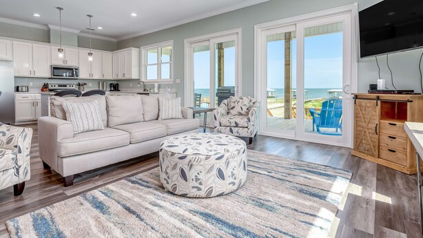 A spacious living area with a sofa, ottoman, and a television. - Idyllic, dog-friendly Bay Front Island home with pool, Gulf view & large decks (Dauphin Island)