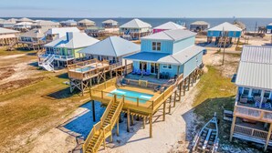 A beachfront property with multiple houses, a swimming pool, and wooden walkways. - Idyllic, dog-friendly Bay Front Island home with pool, Gulf view & large decks (Dauphin Island)