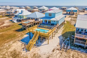A beachfront property with multiple houses, a swimming pool, and wooden walkways. - Idyllic, dog-friendly Bay Front Island home with pool, Gulf view & large decks (Dauphin Island)
