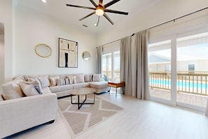 A modern living room with a sectional sofa, a coffee table, a ceiling fan, and a view of a pool through large sliding doors.