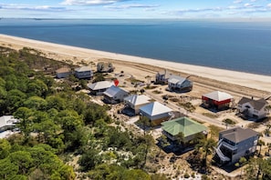 An aerial view of a coastal residential area with houses, a beach, and a lighthouse in the distance.