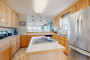 A modern kitchen with wooden cabinets, a stainless steel refrigerator, a built-in stove, and pendant lighting.