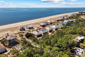 An aerial view of a coastal residential area with houses, a beach, and a clear sky.