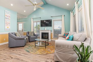 A living room with a fireplace, two sofas, a coffee table, and a TV mounted on the wall. - Gulf-View Home - Bay Views, Free Internet, Central AC, Washer & Dryer (Dauphin Island)