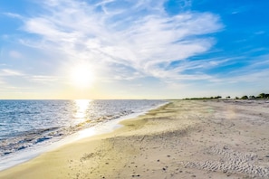 Ein Strand mit klarem Himmel und Sonnenlicht, das sich im Wasser spiegelt.