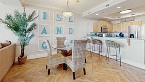 Une cuisine moderne avec des meubles blancs, un réfrigérateur en acier inoxydable et un coin bar agrémenté de chaises en osier.