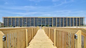 Une promenade en bois mène à un hôtel à plusieurs étages, doté d’un toit plat et de nombreuses fenêtres.