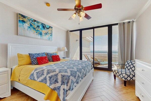 A bedroom with a bed, a ceiling fan, a painting, a balcony with a chair, and a view of the outdoors. - Bright & beachy waterfront condo with pools, tennis, gym, spacious balcony & W/D (Dauphin Island)