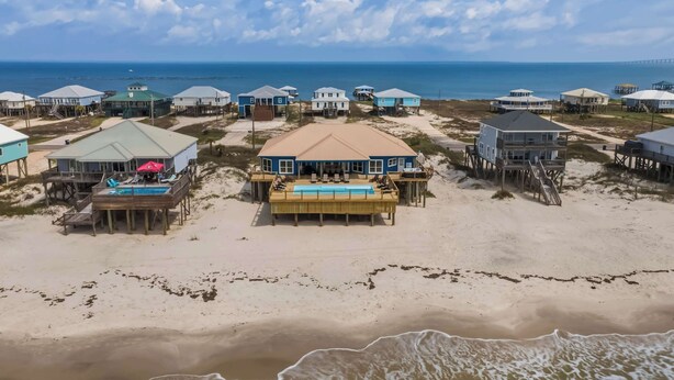 Een strandhuis met meerdere huizen op palen, een zwembad en uitzicht op de oceaan.