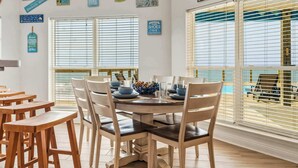 Een eetgedeelte met een ronde tafel, stoelen en uitzicht op het strand door grote ramen.