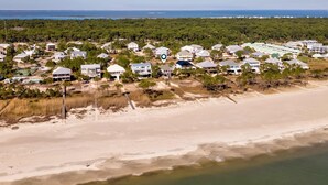 An aerial view of a coastal residential area with houses, a beach, and a forested background. - Tan Lanes! Cozy, affordable and direct access to the beach. (Dauphin Island)