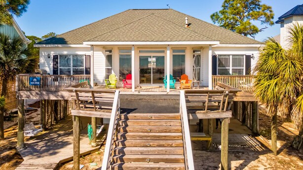 A house with a covered deck, a pool, and a porch with colorful chairs. - Tan Lanes! Cozy, affordable and direct access to the beach. (Dauphin Island)