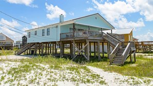 A coastal house with a wooden deck, multiple staircases, and a sandy beach in the foreground. - Welcoming home with WiFi, gulf views & spacious deck - steps to the beach (Dauphin Island)