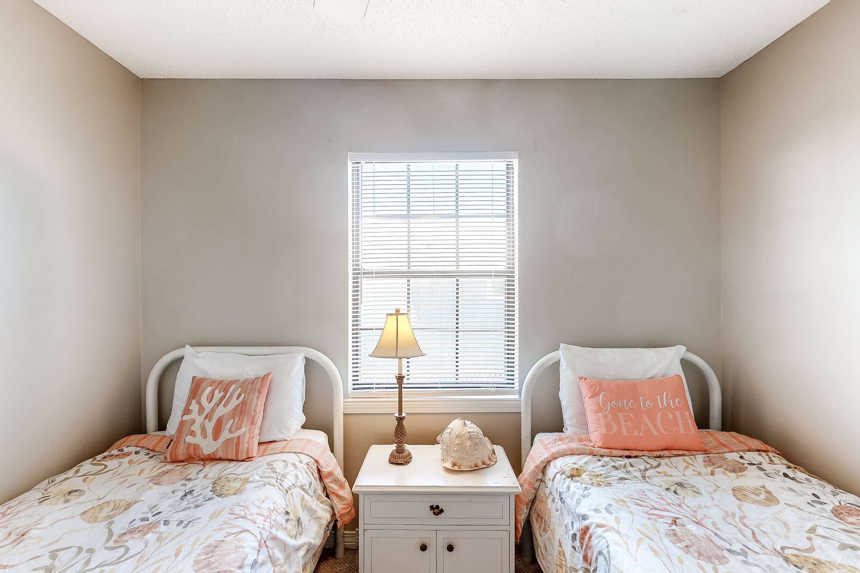 A bedroom with two beds, a nightstand, a lamp, and a window with blinds.